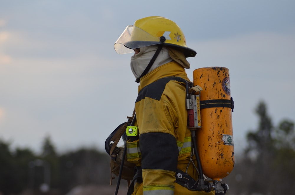 man in yellow hard hat and yellow jacket carrying black dslr camera