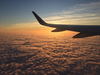 A sleek airplane soaring above fluffy white clouds at sunset, casting a warm golden glow.