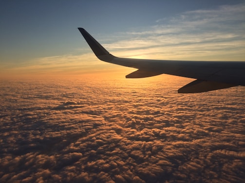 A corporate jet soaring above the clouds during a golden sunset.