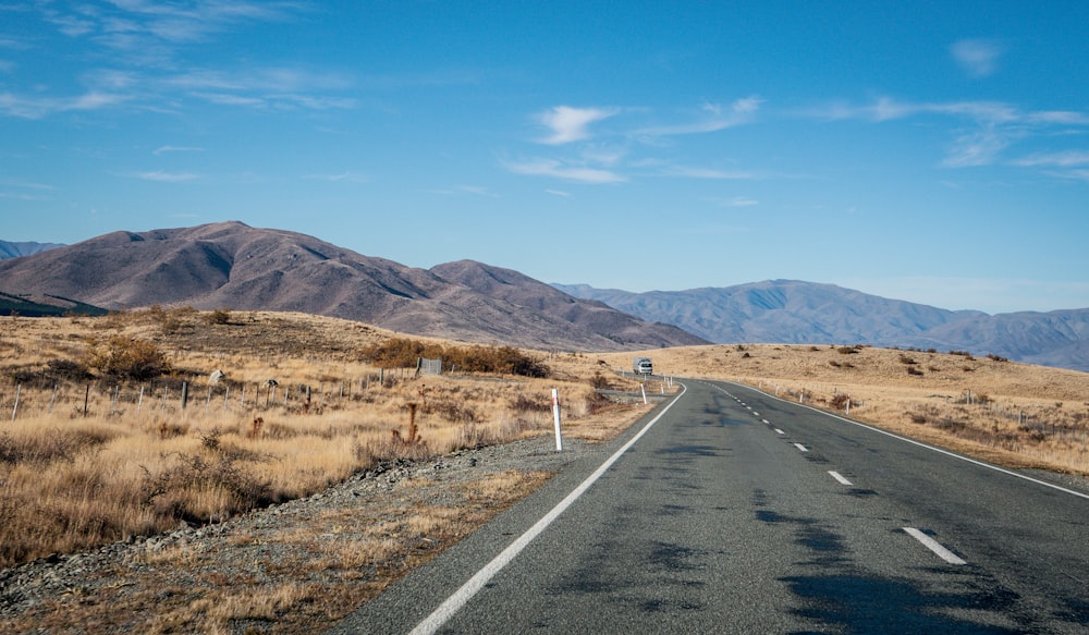 gray asphalt road between brown grass field during daytime