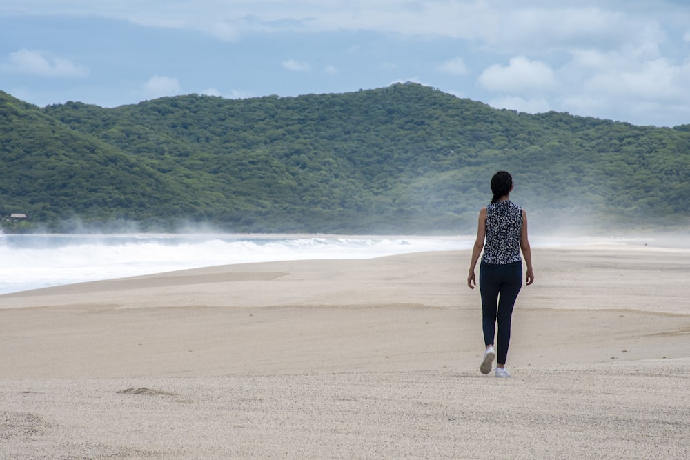 femme en robe noire et blanche marchant sur le bord de mer pendant la journée