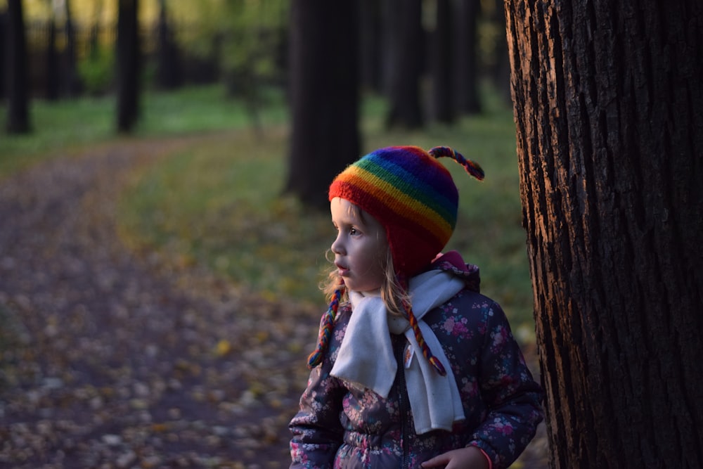 girl in blue and white jacket standing beside tree during daytime