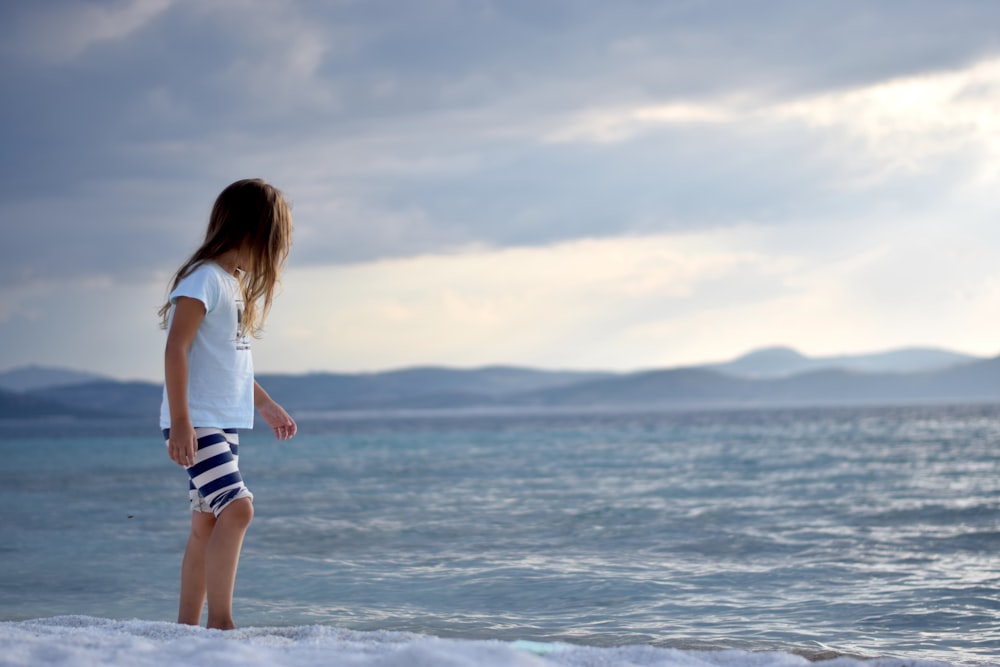 woman in white shirt and blue denim daisy dukes standing on beach during daytime