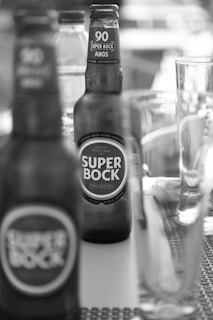 Several bottles of Super Bock beer are placed on a table. The focus is on one bottle in the foreground with another bottle visible in the background. A glass and other beverage containers are also present, contributing to a casual and laid-back atmosphere.