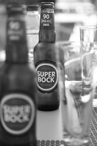 Several bottles of Super Bock beer are placed on a table. The focus is on one bottle in the foreground with another bottle visible in the background. A glass and other beverage containers are also present, contributing to a casual and laid-back atmosphere.