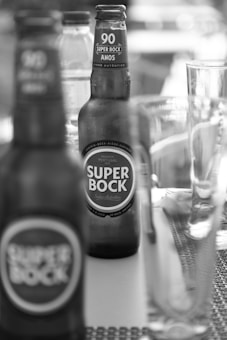 Several bottles of Super Bock beer are placed on a table. The focus is on one bottle in the foreground with another bottle visible in the background. A glass and other beverage containers are also present, contributing to a casual and laid-back atmosphere.