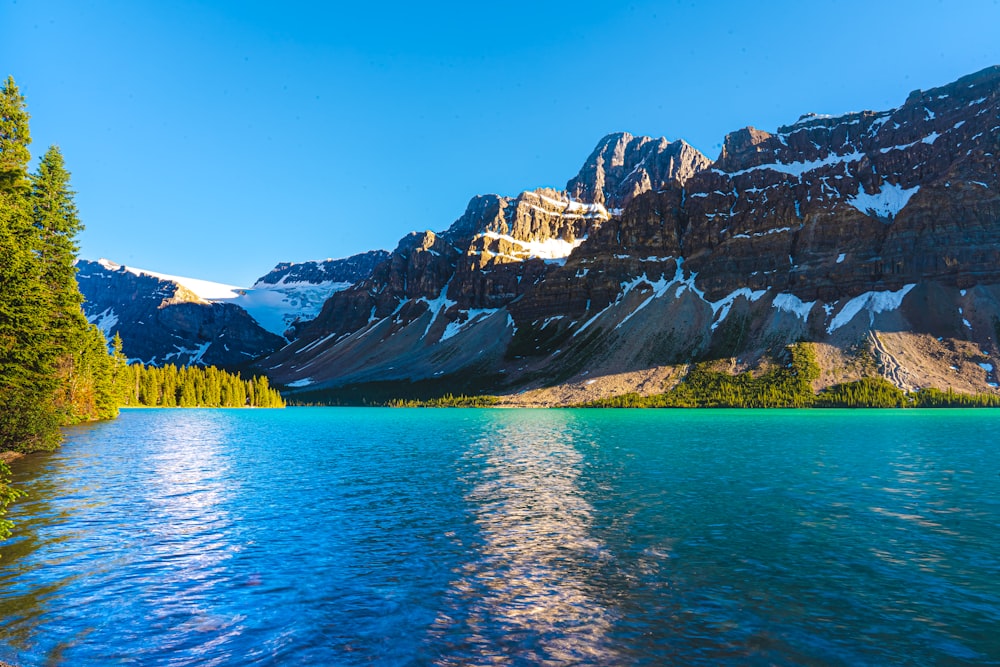 Montagnes brunes et blanches à côté d’un plan d’eau sous un ciel bleu pendant la journée