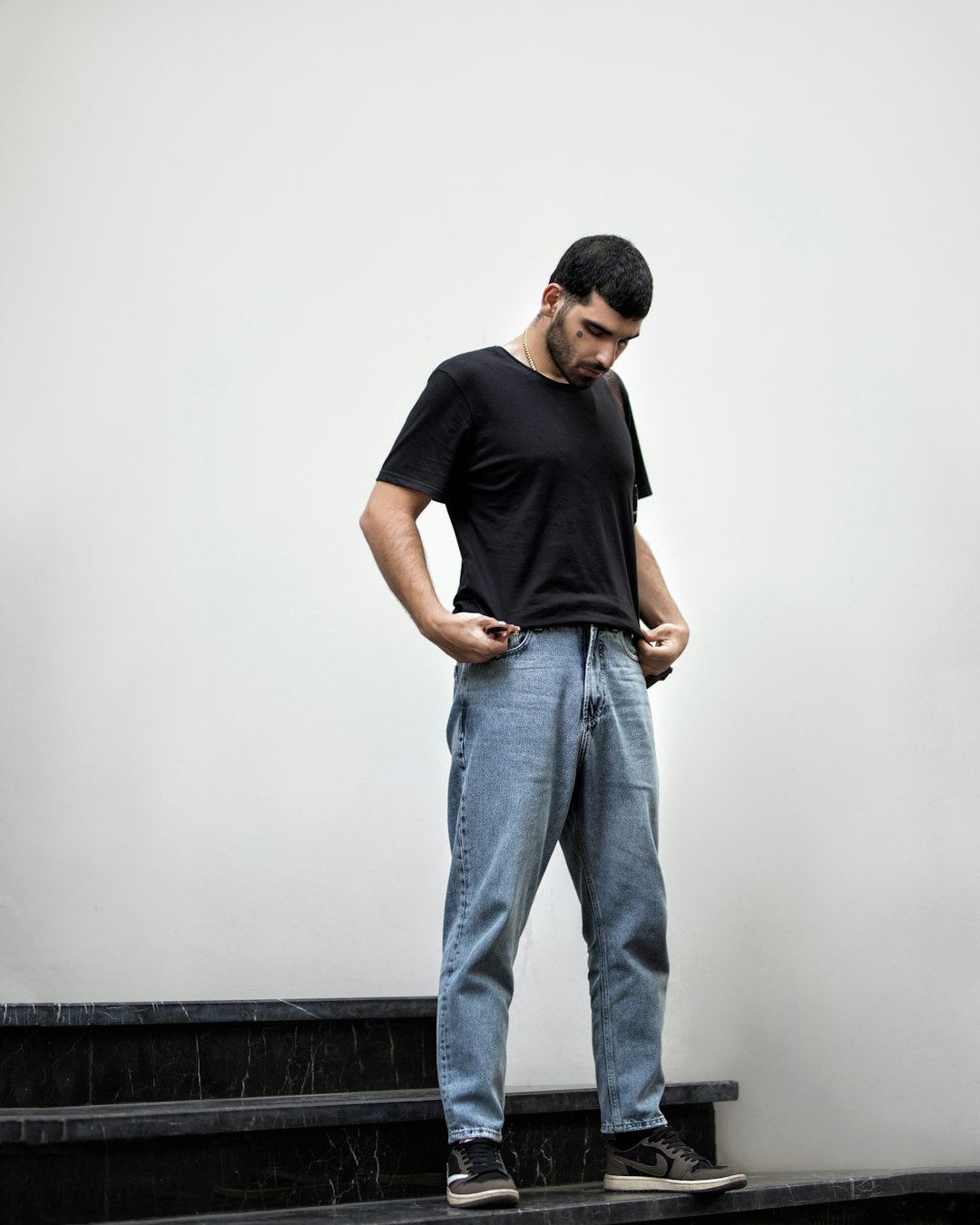 man in black crew neck t-shirt and blue denim jeans standing on black concrete stairs