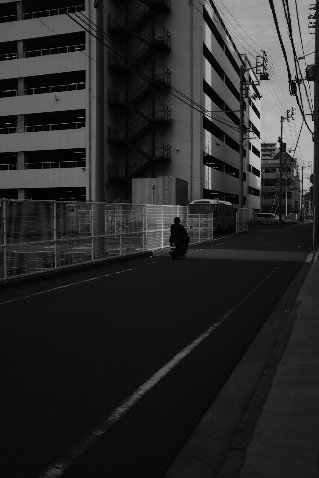 grayscale photo of person walking on sidewalk near building
