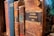 A collection of old, leather-bound books with various titles visible on their spines. The books appear worn and aged, indicating they have been used frequently or are quite old. The focus is on one particular book labeled 'Memorial Administratif 1881,' suggesting a historical or administrative context.