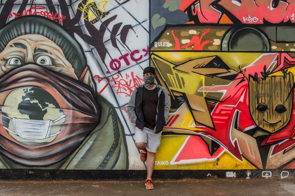 woman in black jacket and white pants standing beside wall with graffiti