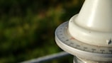 A close-up view of a circular instrument with a scale marked in degrees. The object appears to be a part of a navigational tool, possibly a compass or a theodolite. It is set against a blurred green background, suggesting an outdoor setting.