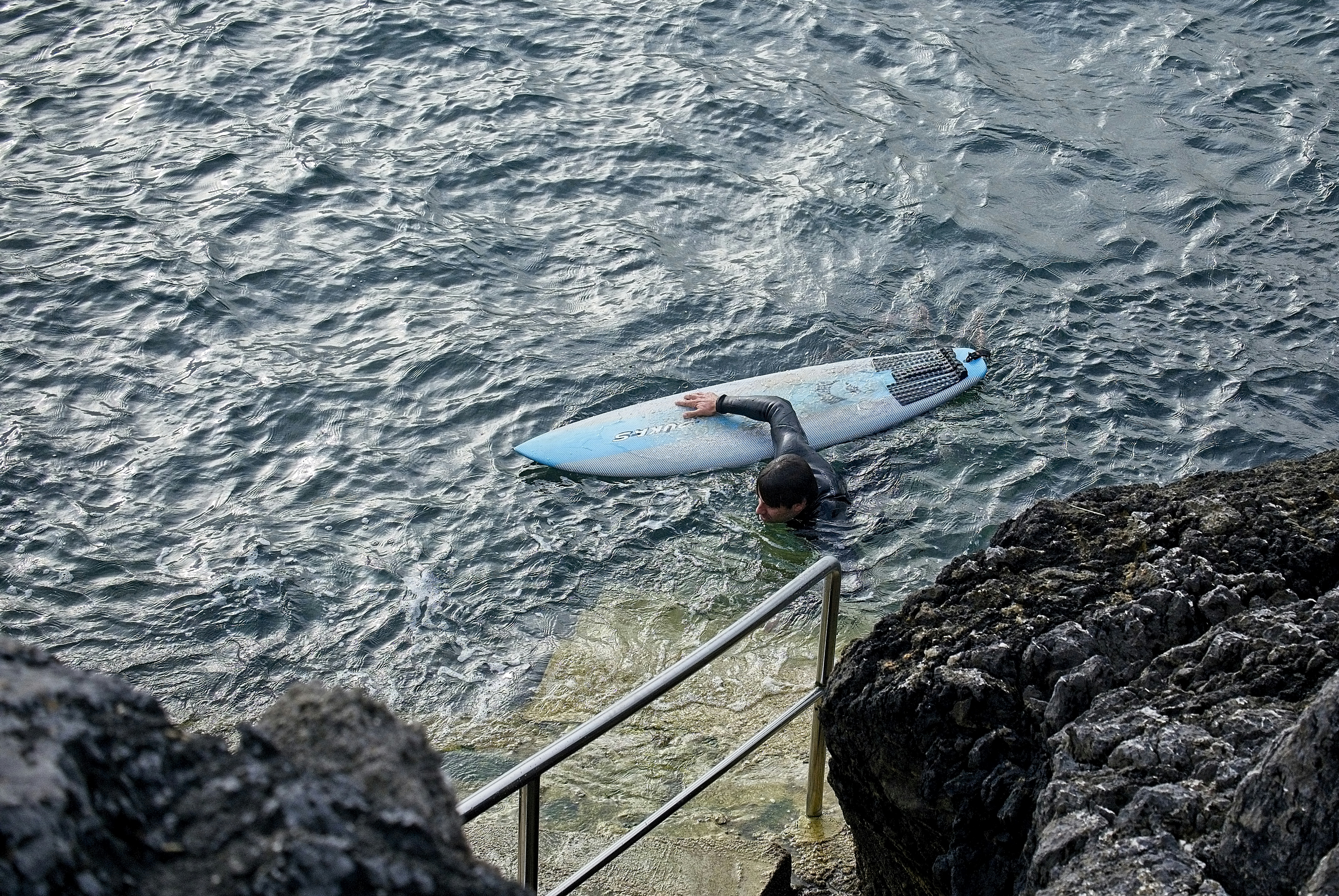 Blue and white surfboard on gray rock near body of water during daytime ...