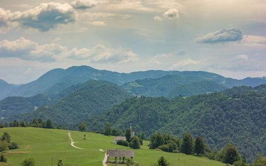 green grass field near green mountains under white clouds during daytime in Cerkno Slovenia