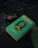 A green book with the title 'Harry Potter and the Order of the Phoenix' by J.K. Rowling, featuring a Slytherin house emblem. The book is placed on a dark surface with a green glass potion bottle and a dark wax-sealed letter nearby, surrounded by black fabric and twigs.