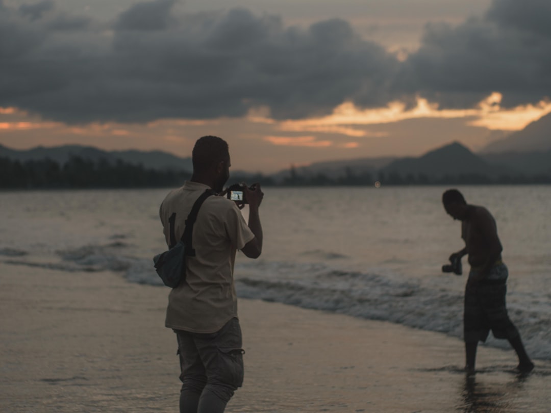 man in brown jacket standing on beach during sunset