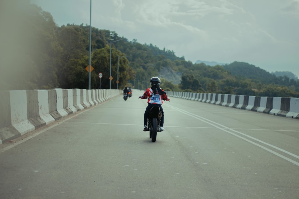 man in red jacket riding motorcycle on gray concrete bridge during daytime