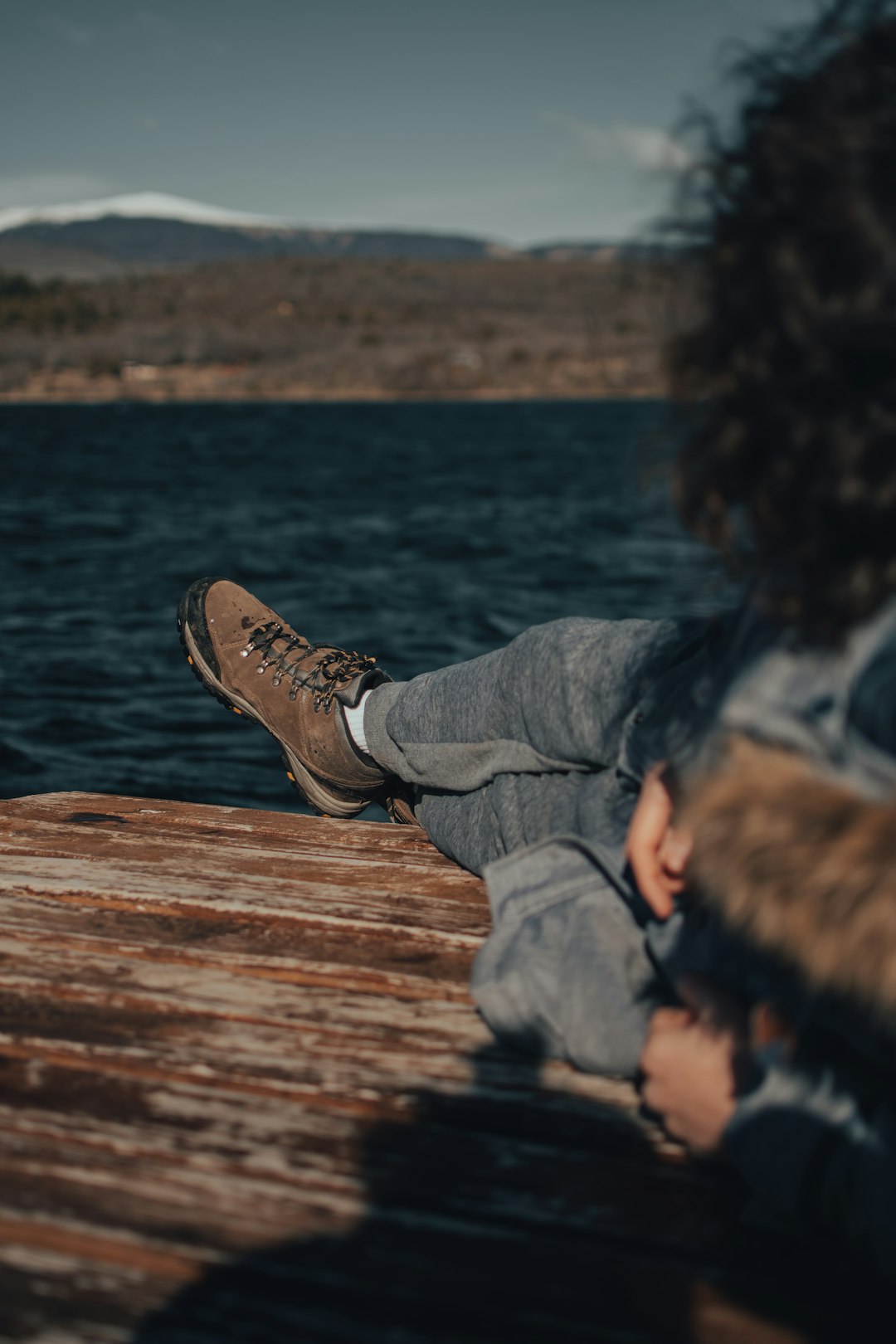 person in gray denim jeans and brown hiking shoes sitting on brown wooden dock during daytime
