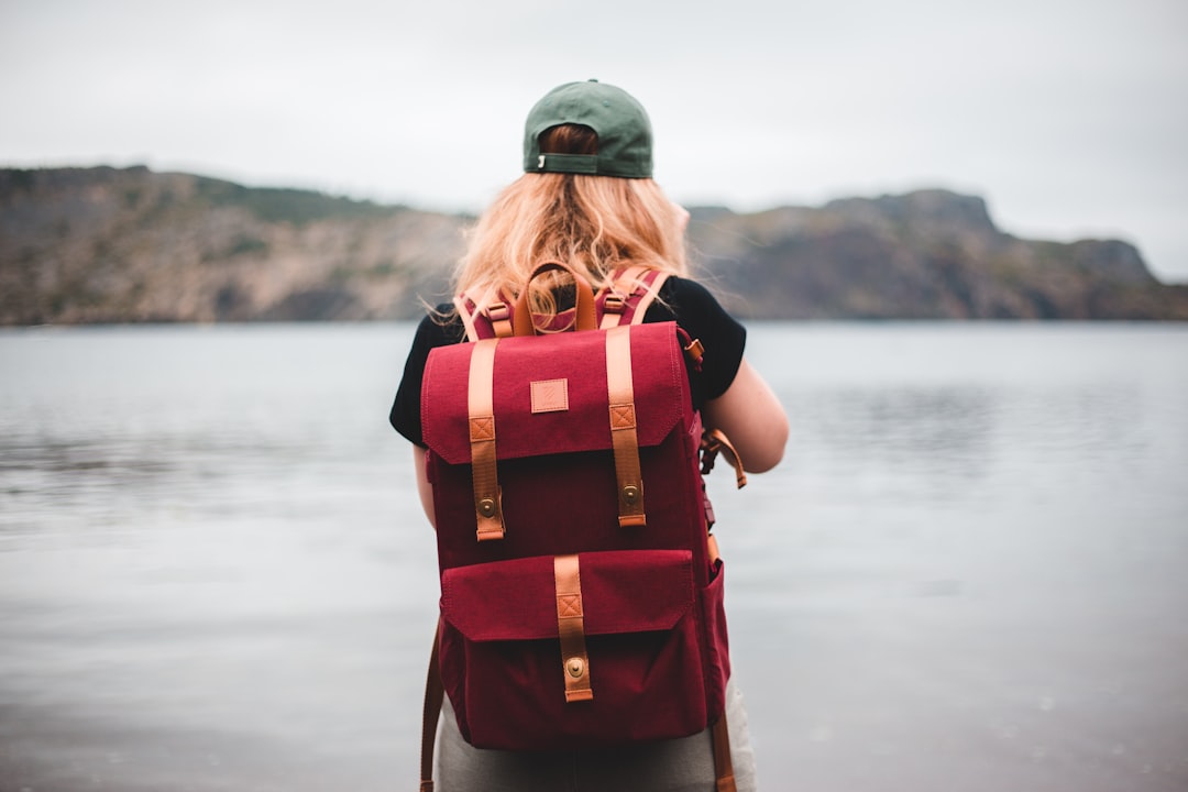 woman in red and black backpack standing on shore during daytime