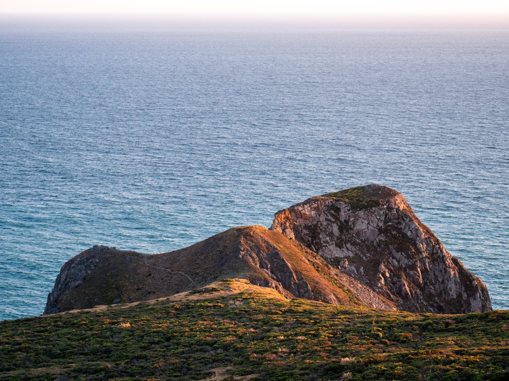 brown and green mountain beside blue sea during daytime