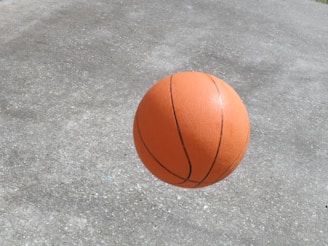 A basketball is captured mid-air against a textured concrete surface. The ball features a classic orange color with black seams and appears to be in motion, suggesting an active or dynamic scene.