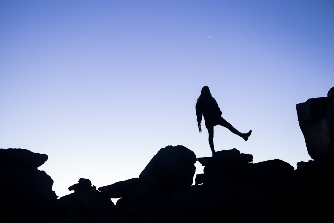 silhouette of woman standing on rock formation during daytime