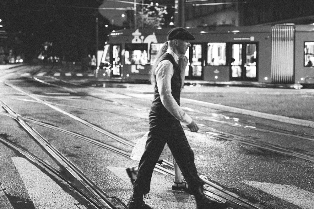 homme en t-shirt et pantalon marchant sur une voie piétonne en niveaux de gris photographie