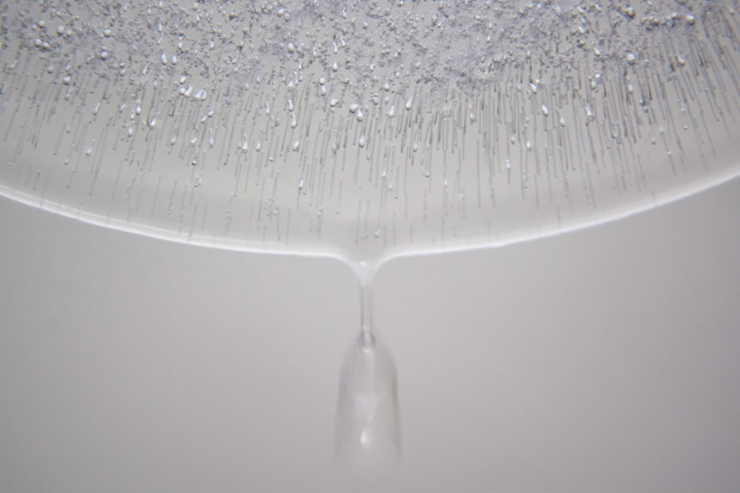 The image features a close-up of a transparent liquid substance forming droplets and lines, likely due to condensation or dripping. The top part is densely populated with the droplets clinging to a surface, creating a pattern reminiscent of stalactites.