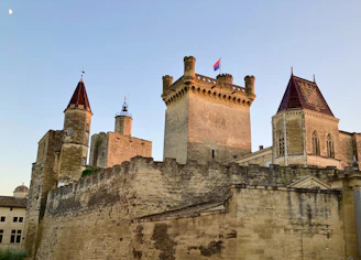 A tall Minecraft castle with stone walls, blue flags, and glowing windows at sunset.