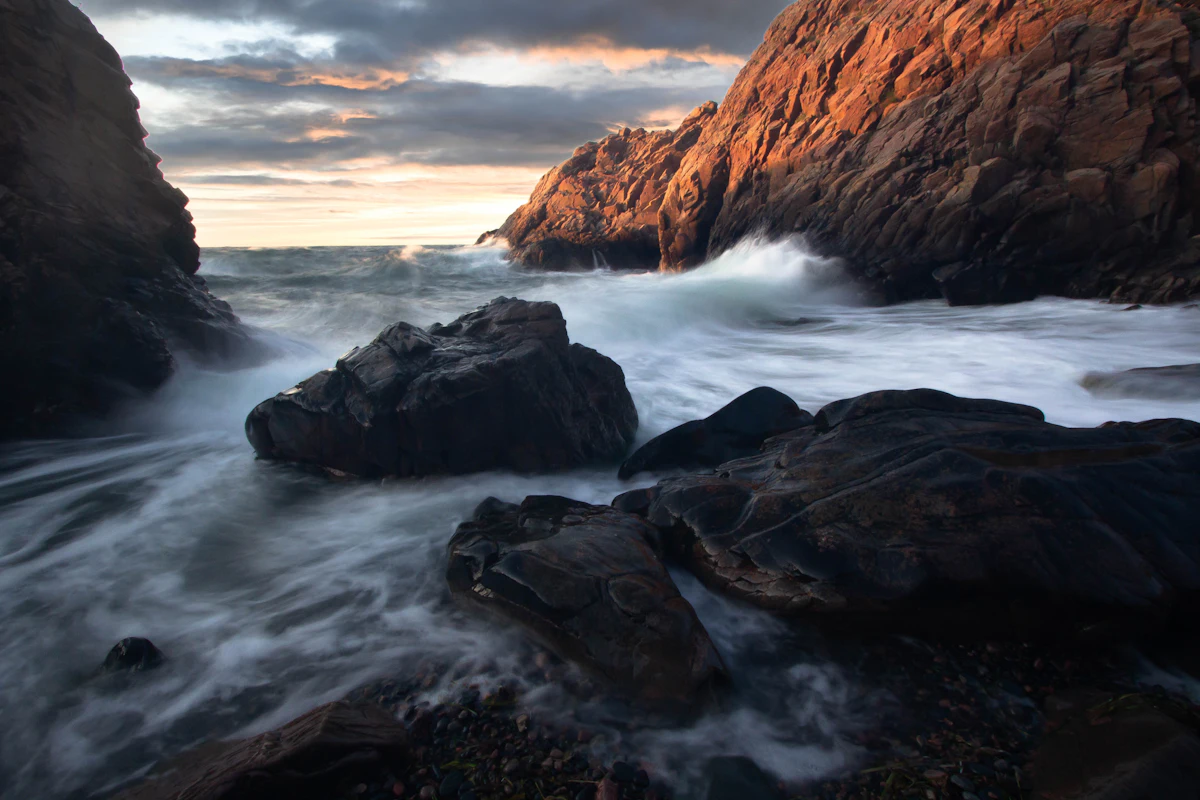 Waves breaking over boulders in a rocky cove near Mölle, under an evening sky