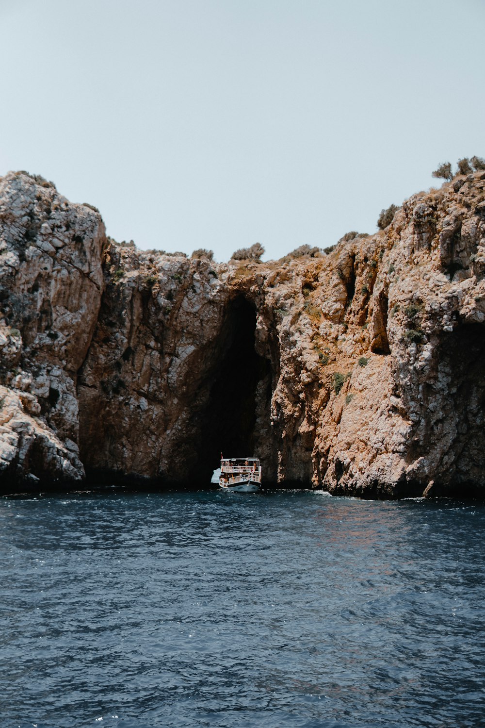 white boat on sea near brown rock formation during daytime