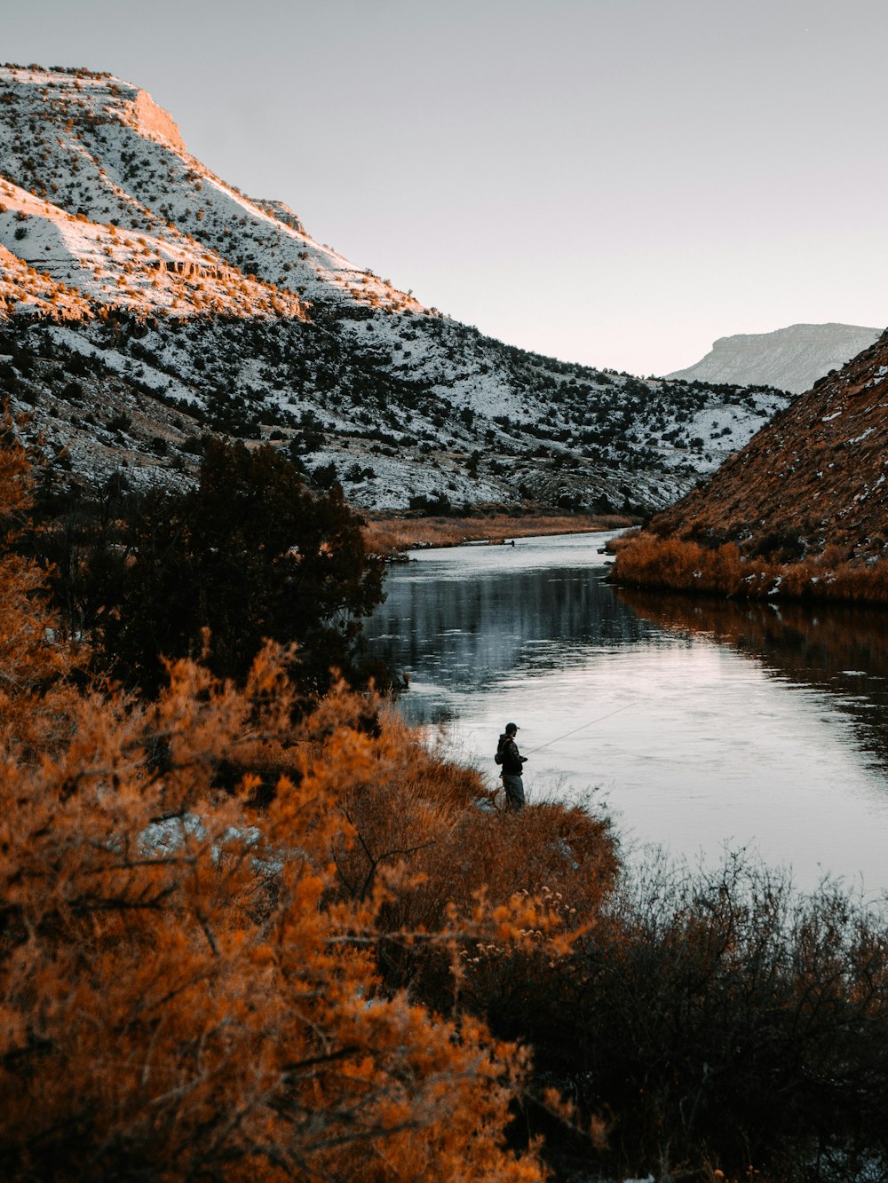 Person, die tagsüber auf dem See in der Nähe eines schneebedeckten Berges steht