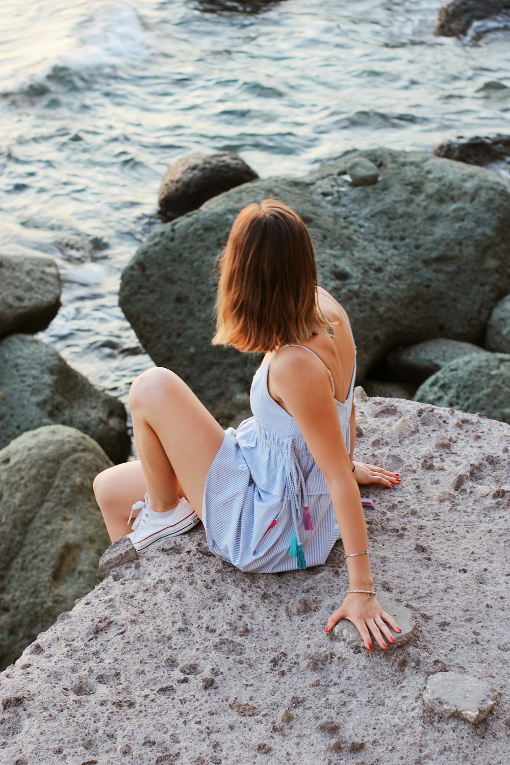 woman in white sleeveless dress sitting on rocky shore during daytime