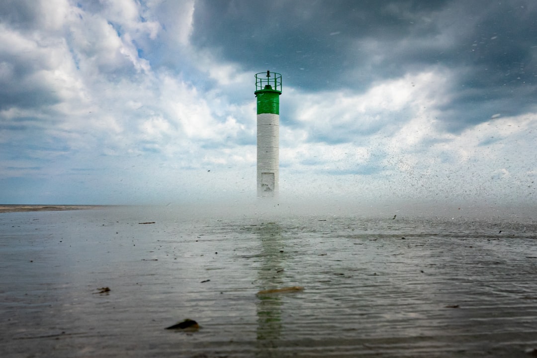 green and white lighthouse on body of water under cloudy sky during daytime