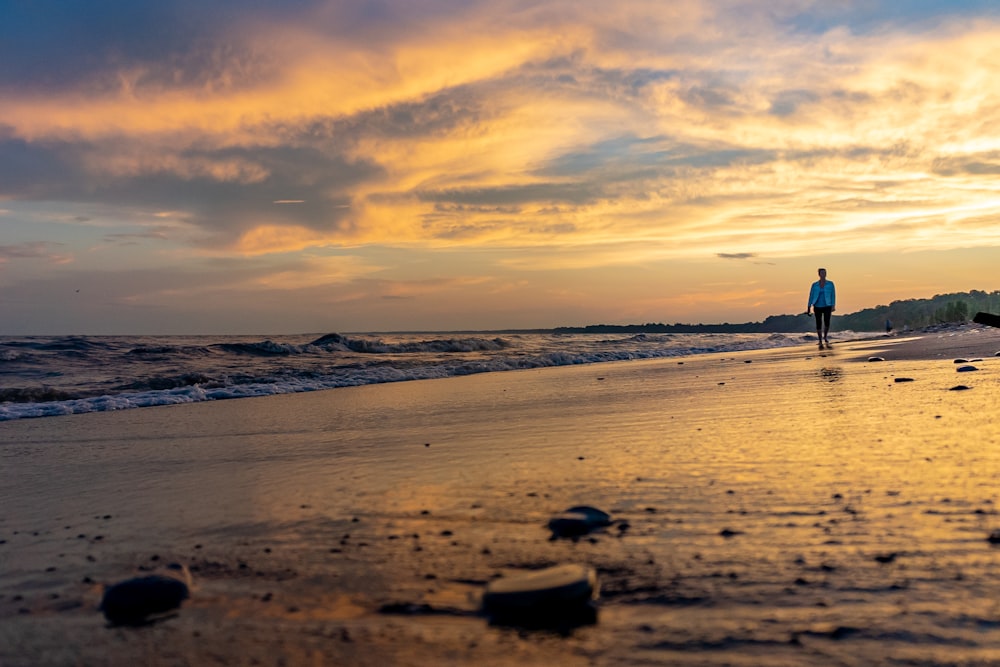 silhueta da pessoa em pé na praia durante o pôr do sol