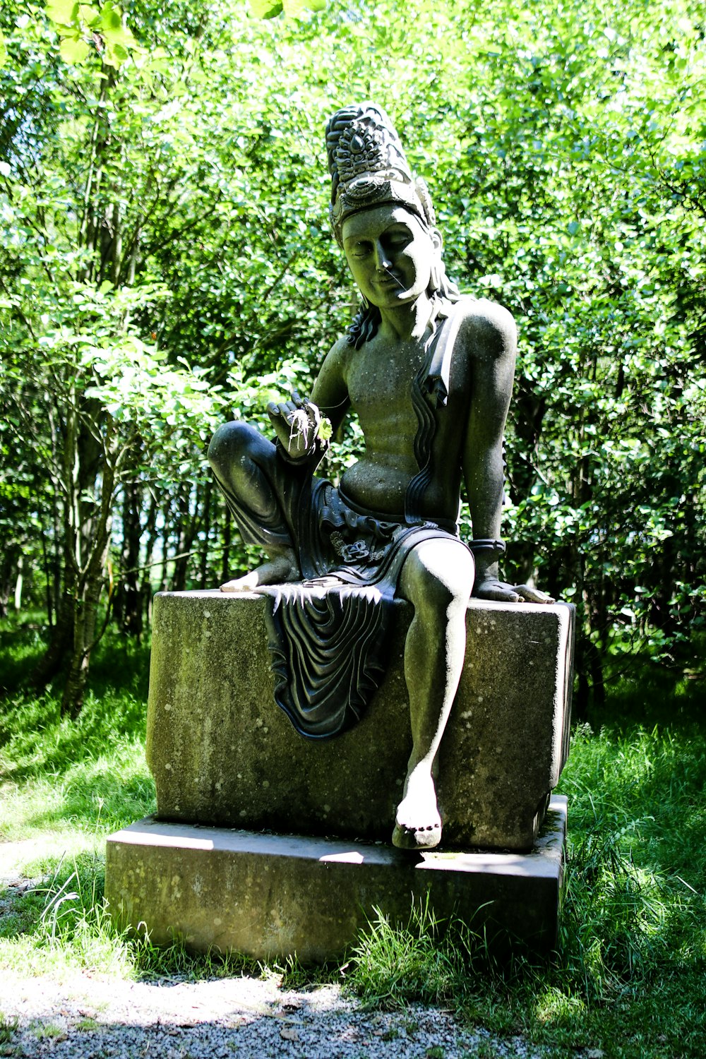 green statue of a man sitting on a rock
