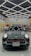 A dark-colored car is parked inside a showroom with a patterned ceiling of bright fluorescent lights. The showroom features a variety of colorful wraps or stickers displayed on the walls and a prominent sign reading 'Tatlises.Sticker' with a multicolored logo. The car has distinctive racing stripes and a reflective surface showing light patterns.