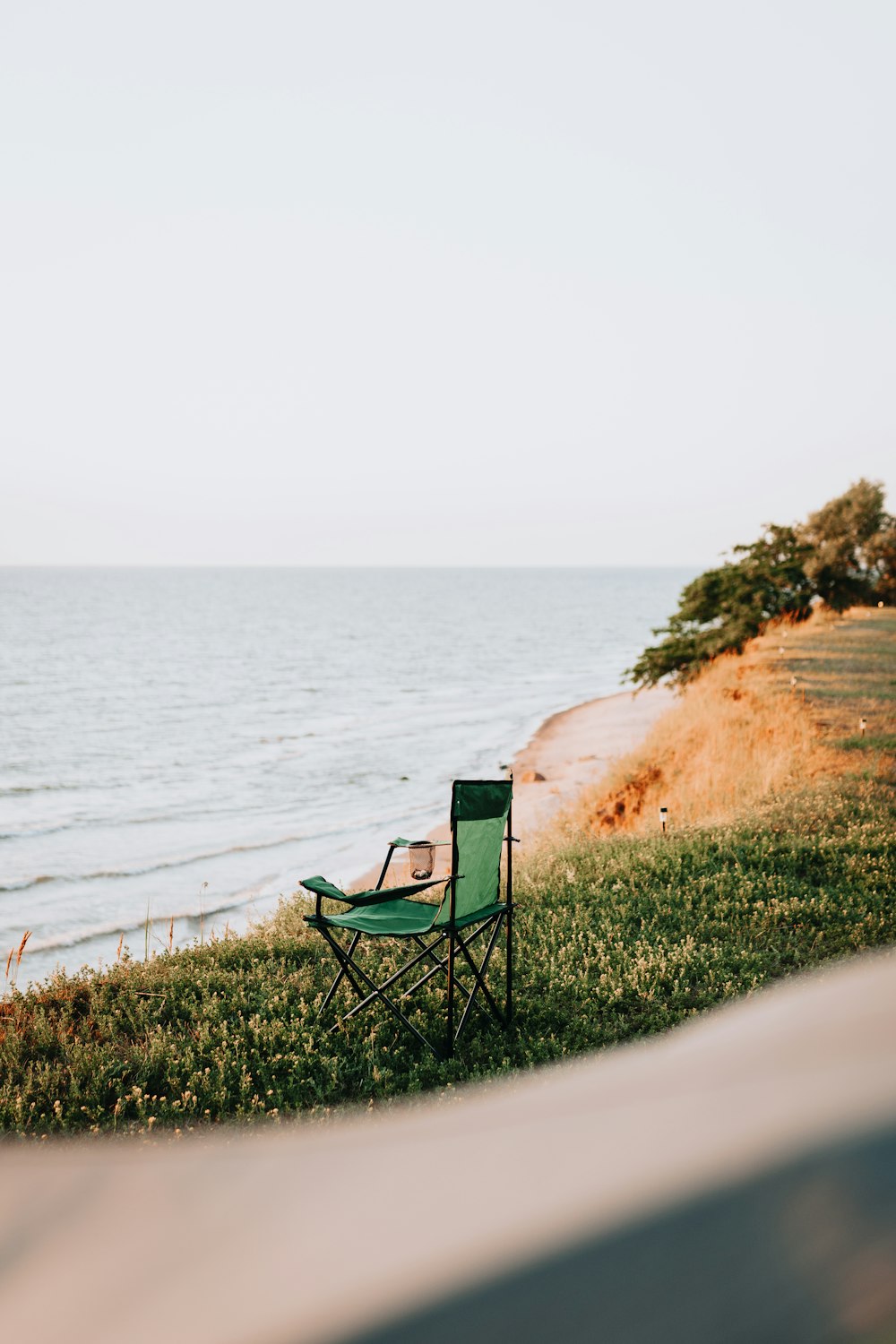 green and black camping chair on brown sand near body of water during daytime