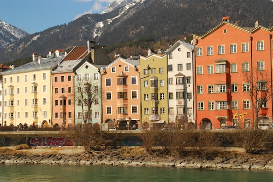 brown and white concrete building beside river during daytime in Colourful Houses Innsbruck Austria