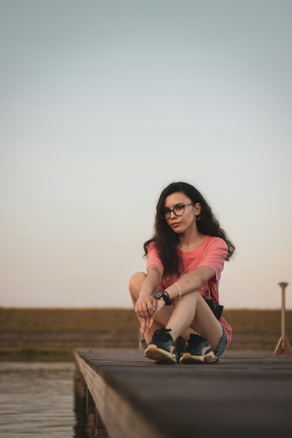 woman in red shirt and black shorts sitting on brown field during daytime