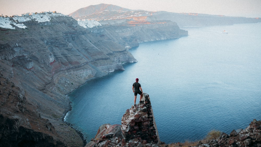 man in black shirt standing on rock formation near body of water during daytime