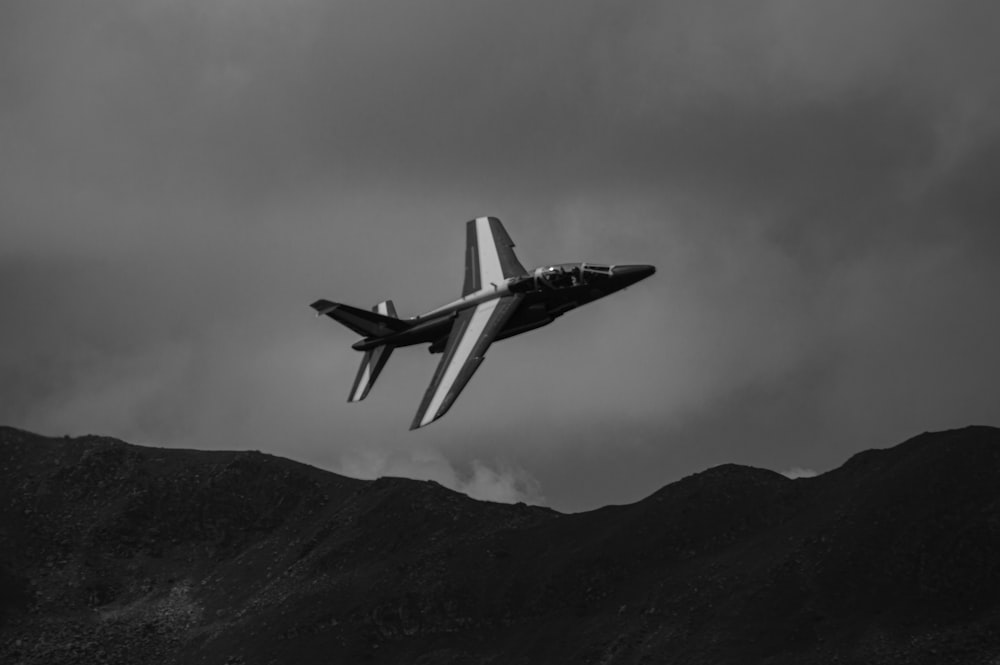 Photo en niveaux de gris d’un avion de chasse survolant la montagne