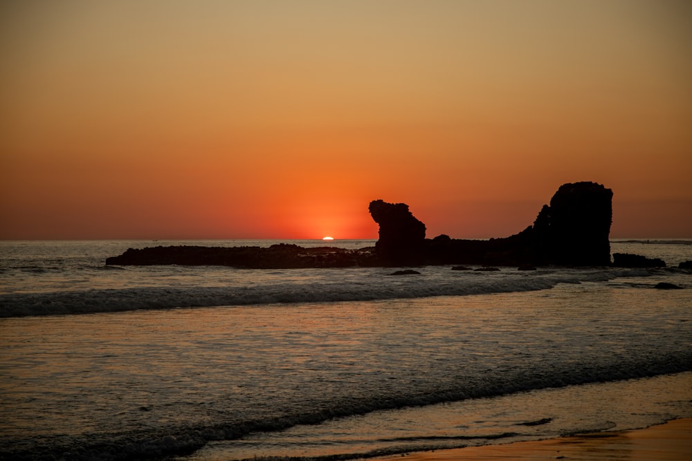 silhouette de formation rocheuse sur la mer pendant le coucher du soleil