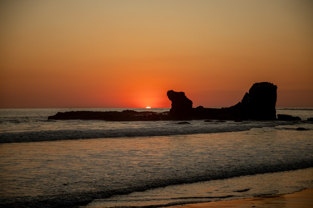 silhouette of rock formation on sea during sunset