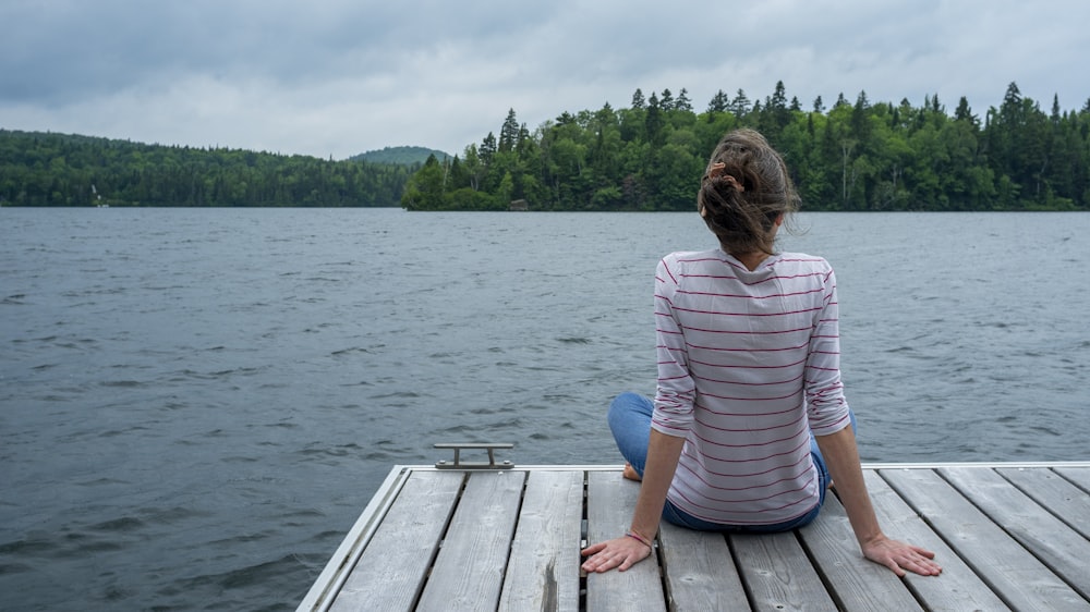 a woman sitting on a dock looking at the water