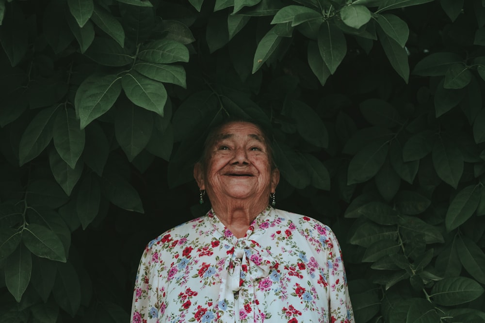 woman in white red and green floral button up shirt standing near green plant