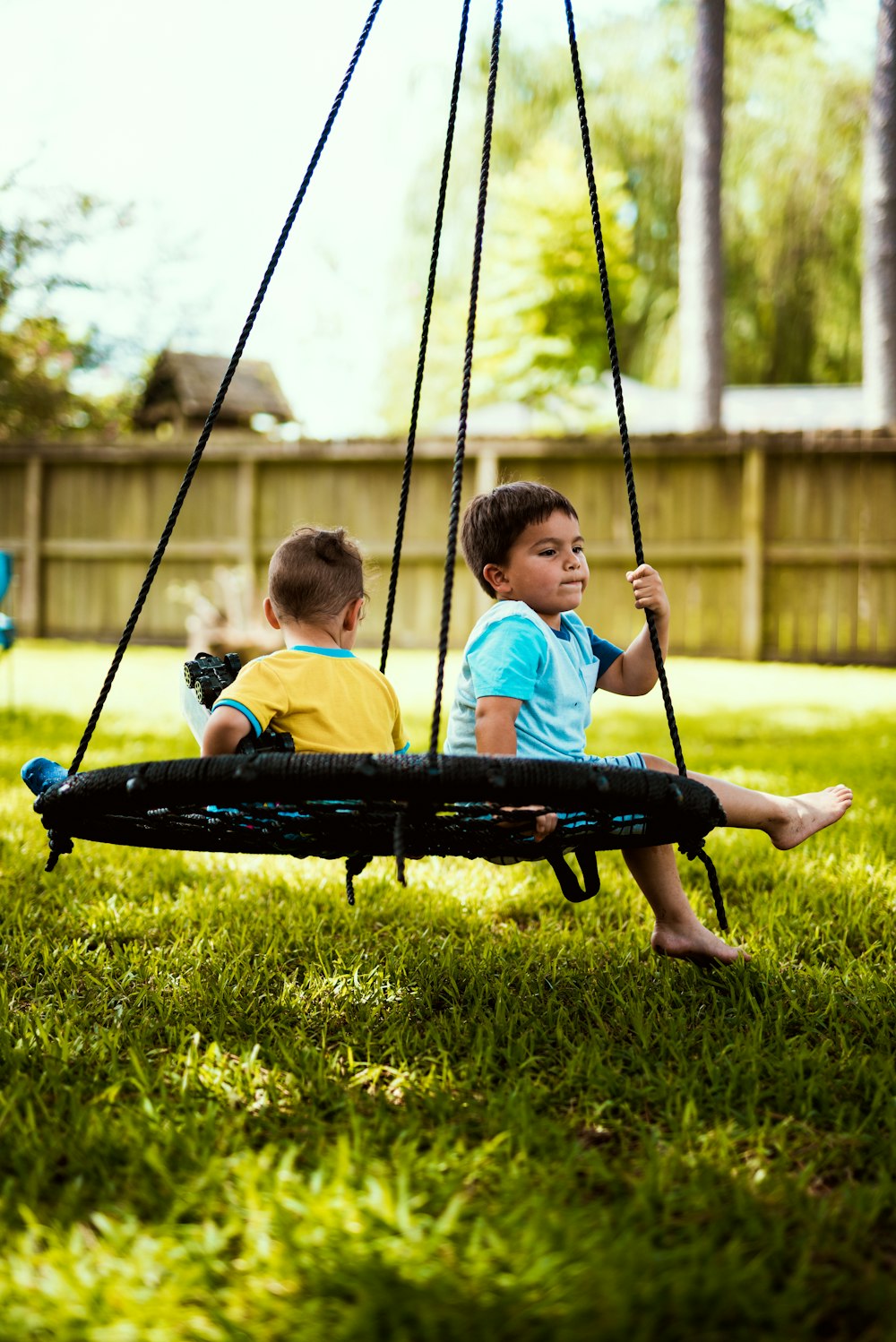 2 boys sitting on blue hammock during daytime
