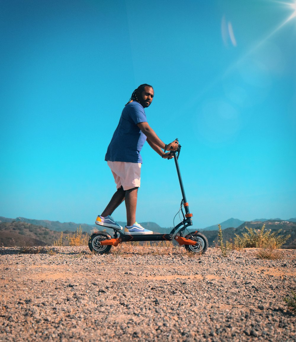 man in blue t-shirt and white shorts riding red and black kick scooter during daytime