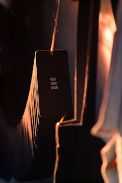 A set of black cards hanging from a string, with the text 'REST YOUR BRAIN' printed on the visible card. The scene is dimly lit with warm light creating a moody ambiance and casting long shadows.