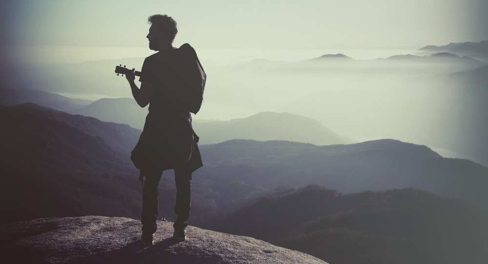 silhouette of man holding camera on top of mountain during daytime